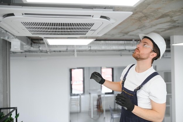 Jeune réparateur réparant l'unité de climatisation de plafond