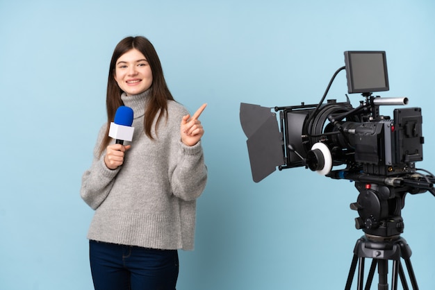 Jeune reporter femme tenant un microphone et rapportant des nouvelles pointant le doigt sur le côté