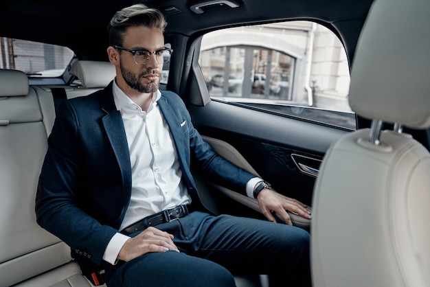 Jeune et réussi. Beau jeune homme en costume complet à l'écart alors qu'il était assis dans la voiture