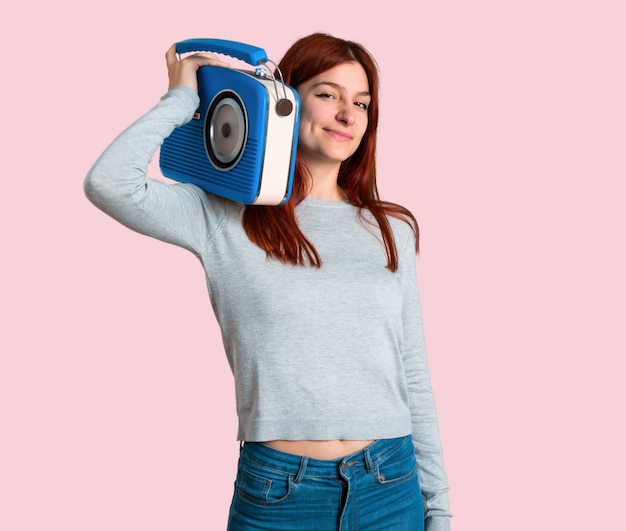 Jeune rousse tenant une radio vintage bleue sur fond rose isolé