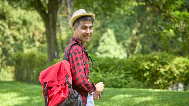 Un jeune routard asiatique tenant une caméra debout dans un parc naturel.