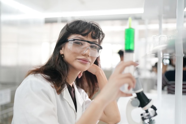 Jeune scientifique en blouse blanche travaillant avec un microscope binoculaire dans le laboratoire de science des matériaux