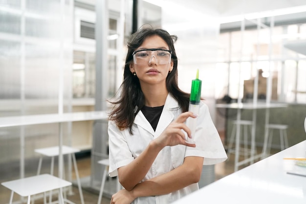 Jeune scientifique en blouse blanche travaillant avec un microscope binoculaire dans le laboratoire de science des matériaux