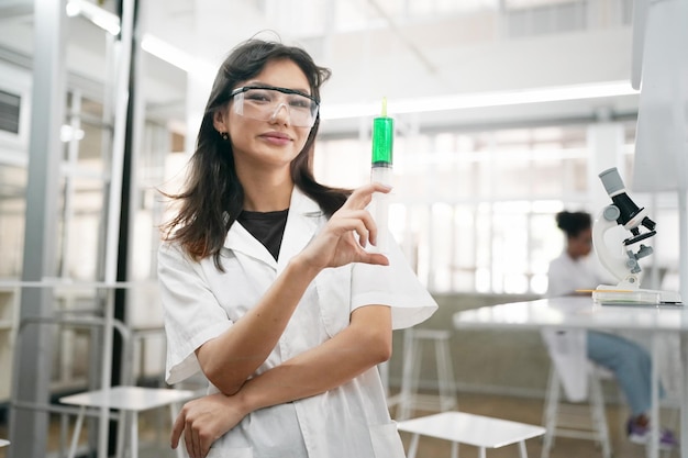 Jeune scientifique en blouse blanche travaillant avec un microscope binoculaire dans le laboratoire de science des matériaux