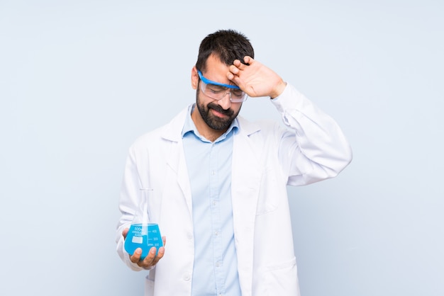 Jeune scientifique tenant une fiole de laboratoire sur un mur isolé avec expression fatiguée et malade