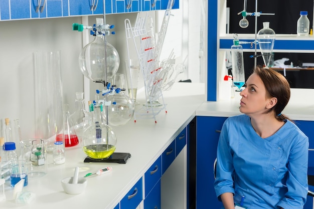 Une jeune scientifique en uniforme examine des flacons après avoir effectué des recherches en laboratoire. Concept de soins de santé et de biotechnologie