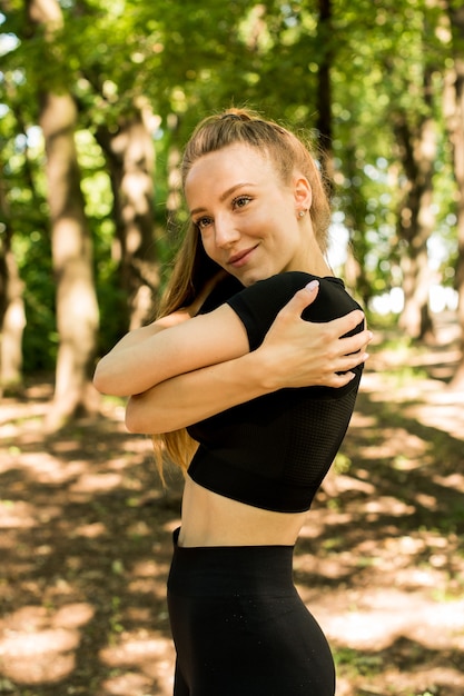 Jeune séance d'entraînement féminine avant la séance d'entraînement de remise en forme dans le parc. Jeune femme en bonne santé se réchauffant à l'extérieur. Elle étire son dos