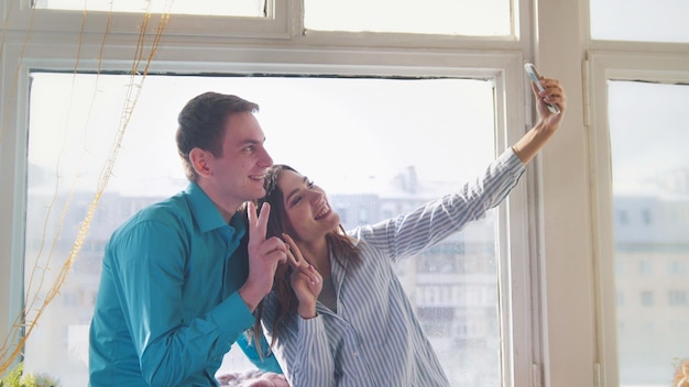 Jeune et séduisant homme et femme faisant un selfie assis à la fenêtre