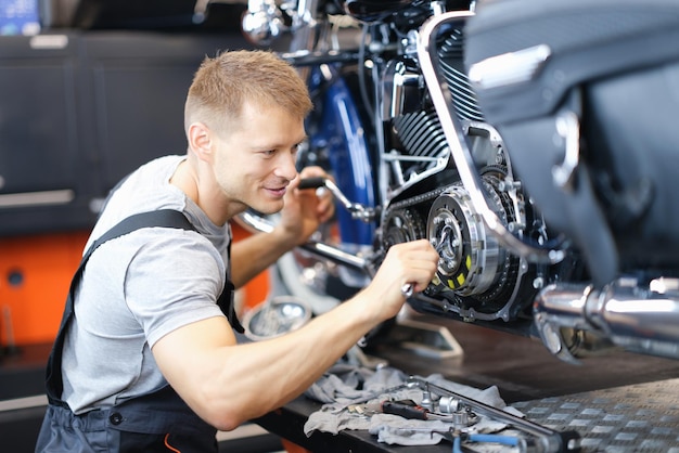 Un jeune serrurier démonte le moteur de la moto sur un banc dans un garage