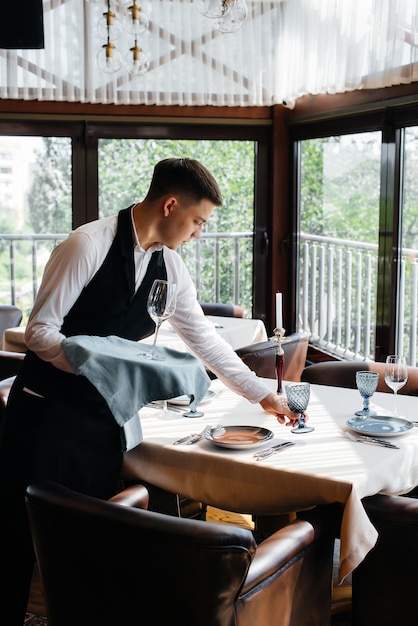Un jeune serveur masculin dans un uniforme élégant est occupé à servir la table dans un beau restaurant gastronomique. Activité de restauration, du plus haut niveau.