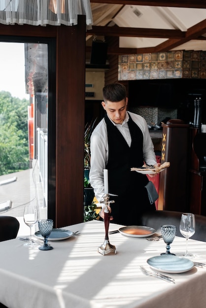 Un jeune serveur masculin dans un uniforme élégant est occupé à servir la table dans un beau restaurant gastronomique Un restaurant de haut niveau Service de table dans le restaurant
