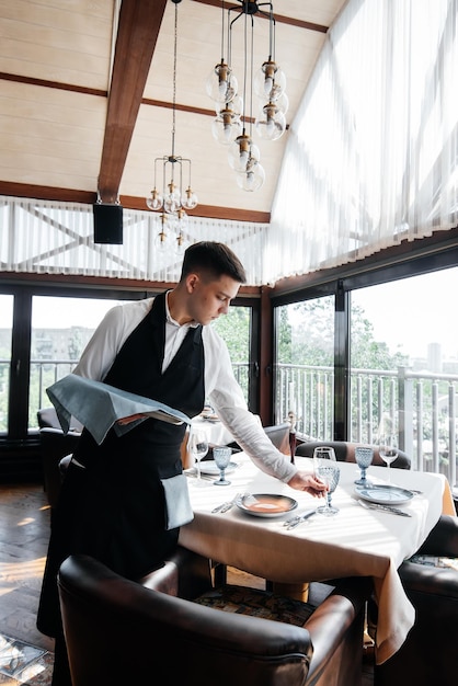 Un jeune serveur masculin dans un uniforme élégant est occupé à servir la table dans un beau restaurant gastronomique Un restaurant de haut niveau Service de table dans le restaurant