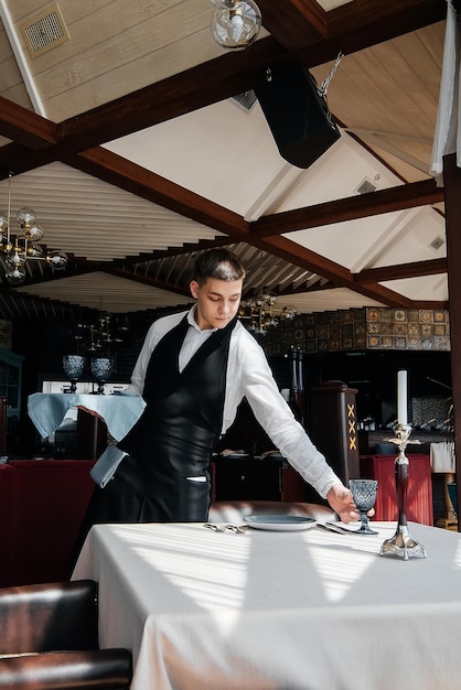 Un jeune serveur masculin dans un uniforme élégant est occupé à servir la table dans un beau restaurant gastronomique Un restaurant de haut niveau Service de table dans le restaurant