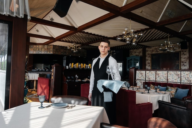 Un jeune serveur masculin dans un uniforme élégant est occupé à servir la table dans un beau restaurant gastronomique Un restaurant de haut niveau Service de table dans le restaurant