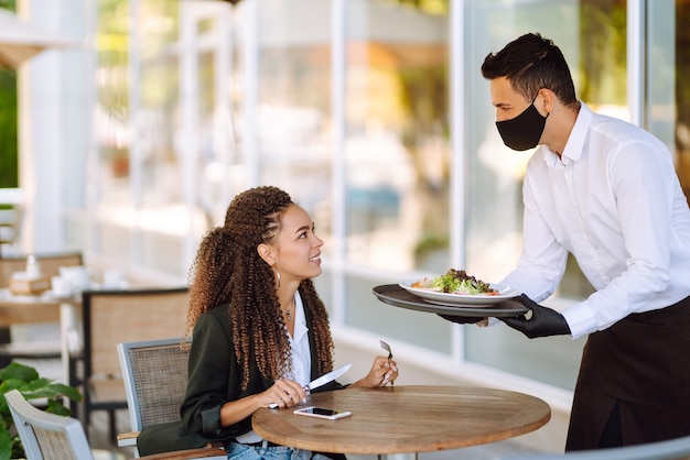 Jeune serveur portant un masque protecteur et des gants avec des repas commandés prêts à servir Covid2019