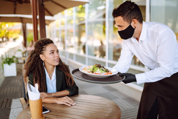 Jeune serveur portant un masque protecteur et des gants avec des repas commandés prêts à servir l'invité Covid2019