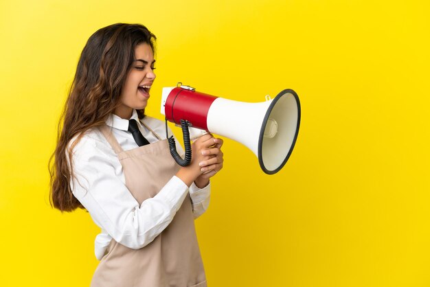 Jeune serveur de restaurant caucasien isolé sur fond jaune criant à travers un mégaphone