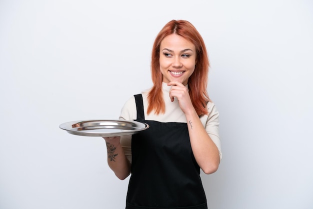 Jeune serveur russe avec plateau isolé sur fond blanc regardant sur le côté et souriant