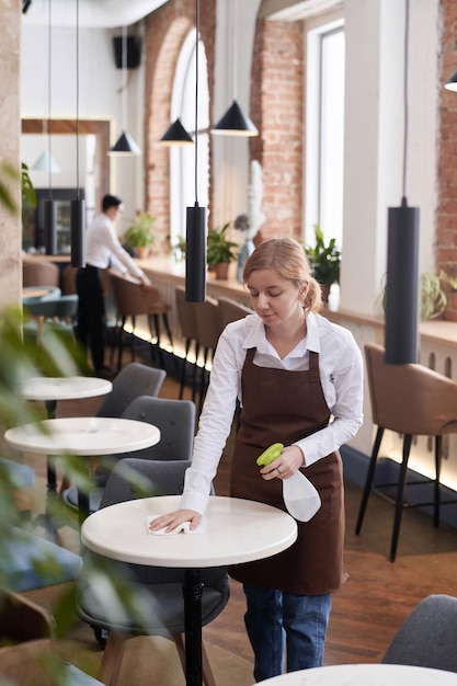 Une jeune serveuse caucasienne nettoie la table.