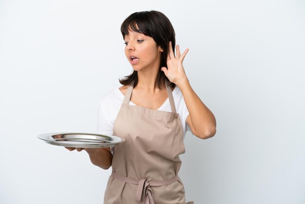 Jeune serveuse avec plateau isolé sur fond blanc écoutant quelque chose en mettant la main sur l'oreille