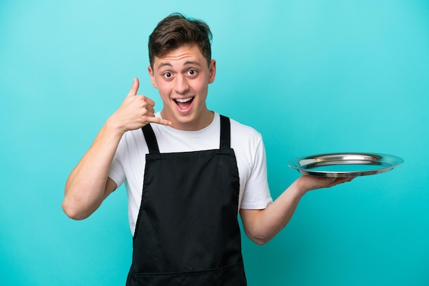 Jeune serveuse avec plateau isolé sur fond bleu faisant un geste de téléphone. Rappelez-moi signe