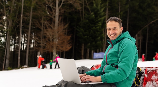 Jeune snowboarder utilisant un ordinateur portable sur une montagne enneigée. Neige blanche et ciel bleu. Copiez l'espace pour la publicité.