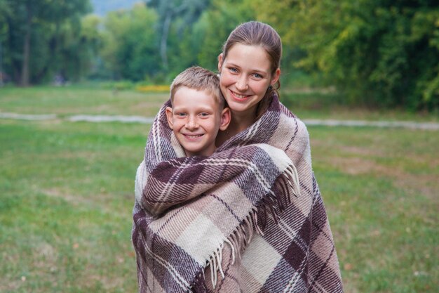 La jeune soeur et le frère se tiennent couverts de plaid dans le parc