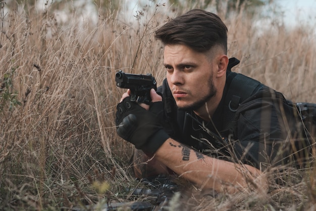 Jeune soldat en uniforme noir couché et visant un pistolet