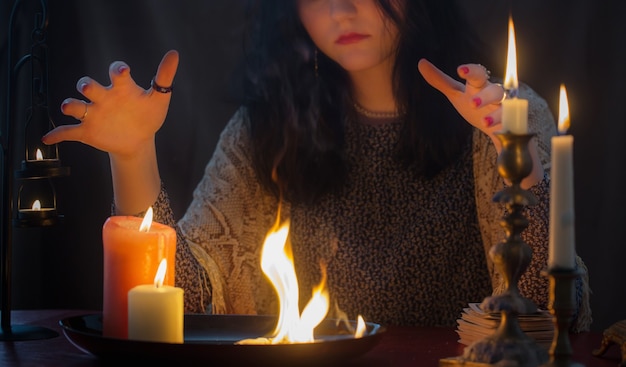 Jeune sorcière avec feu et bougies allumées sur fond sombre