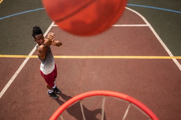 Jeune sportif africain lancer la balle dans le panier en se tenant debout sur le terrain pendant la formation