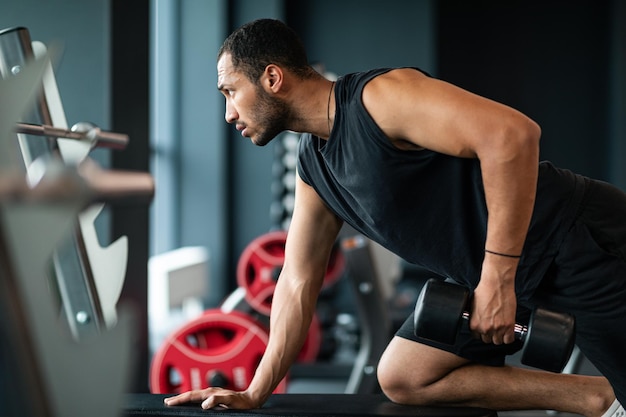 Jeune sportif afro-américain s'entraînant avec haltère à l'intérieur de la salle de sport