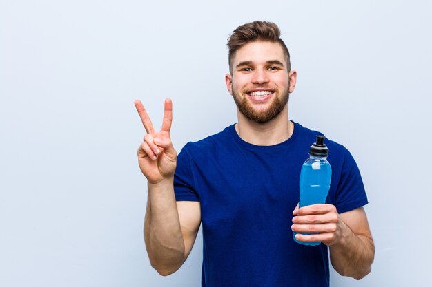 Jeune sportif caucasien tenant une boisson isotonique montrant le numéro deux avec les doigts.