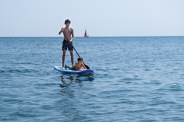 Un jeune sportif avec un enfant navigue sur un sup dans la mer. Concept de mode de vie sain.