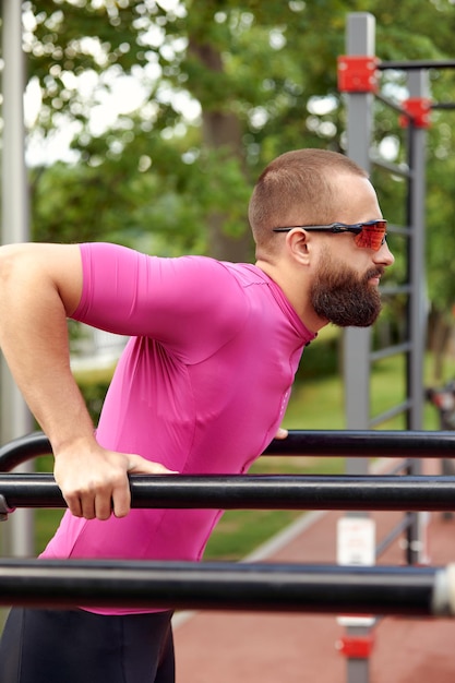 Jeune sportif faisant des pompes sur des barres asymétriques en plein air