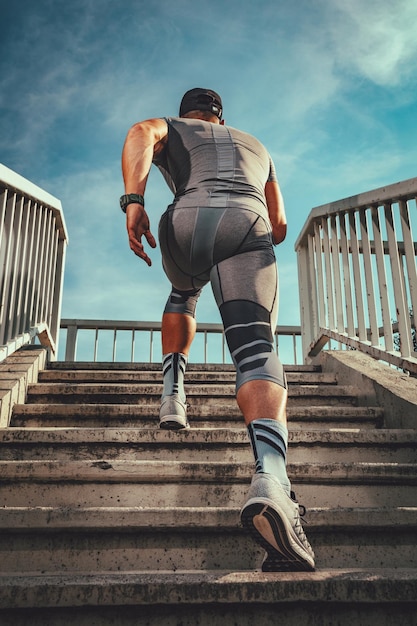 Un jeune sportif musclé monte les escaliers du pont. Vue arrière.