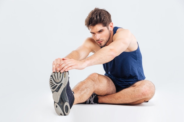 Jeune sportif sérieux travaillant et étirant les jambes sur fond blanc