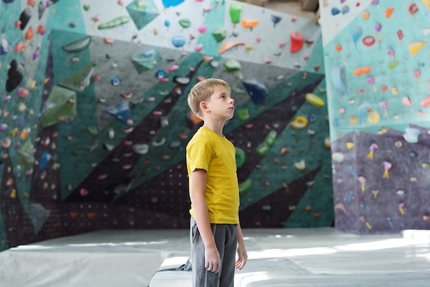 Jeune sportif en vêtements de sport debout au milieu de la pièce pour l'escalade et en regardant l'un des murs