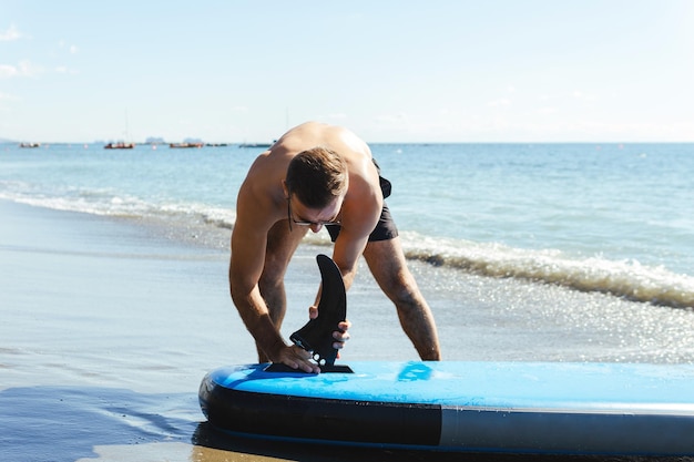 Jeune surfeur installant un paddleboard debout sur une plage