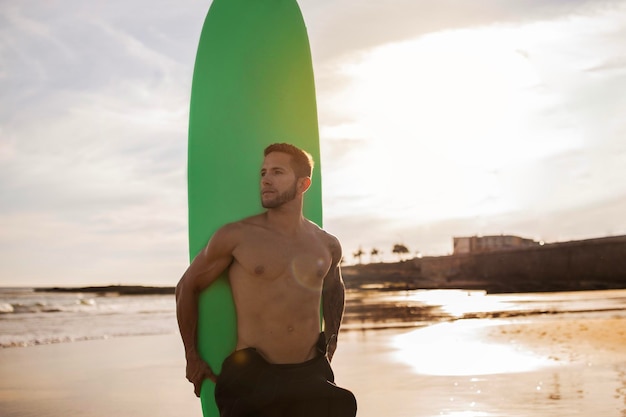 Un jeune surfeur sportif posant avec une planche de surf sur la plage.