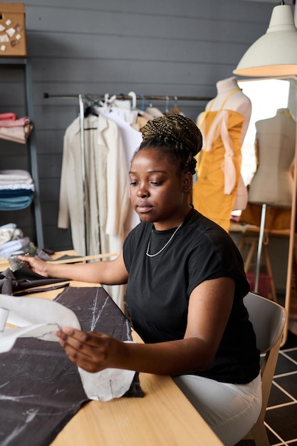 Jeune tailleur sérieux avec motif en papier de vêtements assis sur le lieu de travail