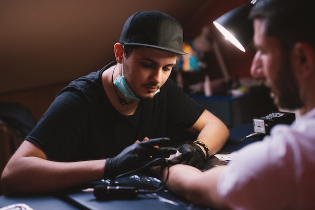 Un jeune tatoueur concentré encrage soigneusement le bras des clients dans sa boutique.