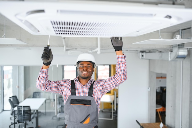 Jeune technicien africain heureux réparant un climatiseur