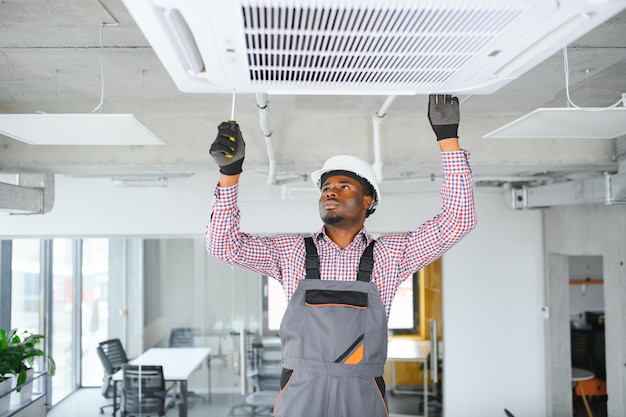 Jeune technicien africain heureux réparant un climatiseur