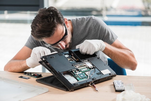 Un jeune technicien fixe un ordinateur sur un bureau en bois.