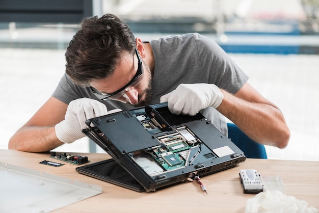 Jeune technicien mâle fixant l&#39;ordinateur sur un bureau en bois