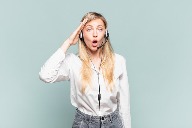 Jeune télévendeuse blonde à l'air heureuse, étonnée et surprise, souriante et réalisant de bonnes nouvelles incroyables et incroyables