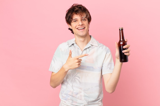 Jeune touriste avec une bière souriant joyeusement se sentir heureux et pointant vers le côté