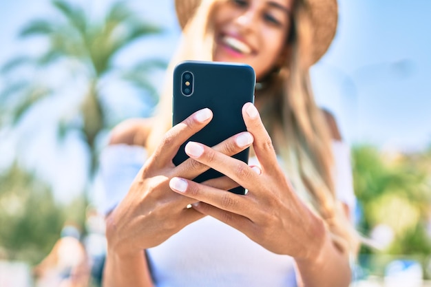 Jeune touriste blonde souriante heureuse à l'aide d'un smartphone dans la ville