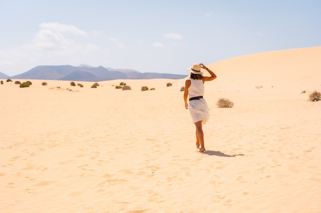 Un jeune touriste caucasien vêtu d'une robe blanche et d'un chapeau marchant dans les dunes du parc naturel de Corralejo, Fuerteventura, Îles Canaries. Espagne