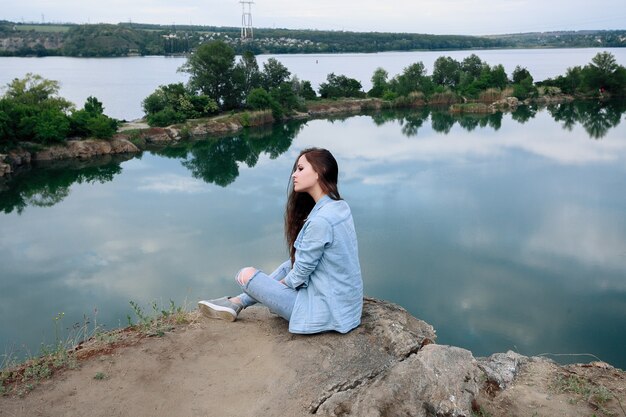 Une jeune touriste est assise sur le dessus du support et regarde un beau paysage. Randonnée femme relaxante au sommet de la falaise en profitant. jolie fille dans des vêtements en jean